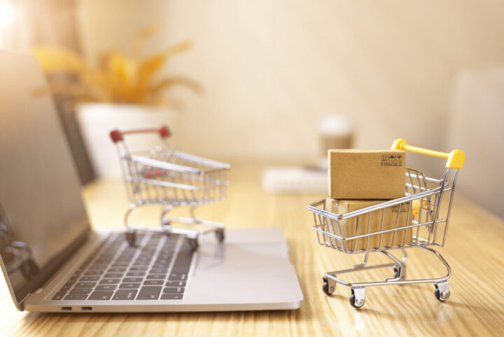 Online shopping and delivery service concept.Brown paper boxs in a shopping cart with laptop keyboard on wood table in office background.Easy shopping with finger tips for consumers.