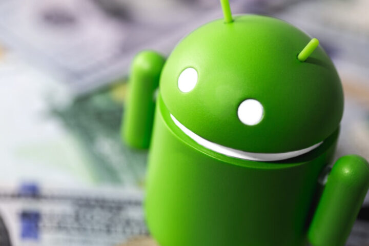 Google Android figure standing on money, dollars. Google Android is the operating system for smartphones, tablet computers, e-books, game consoles, and other devices. Moscow, Russia - March 17, 2019