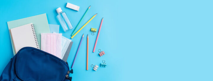 Blue backpack with stationery over blue table background.